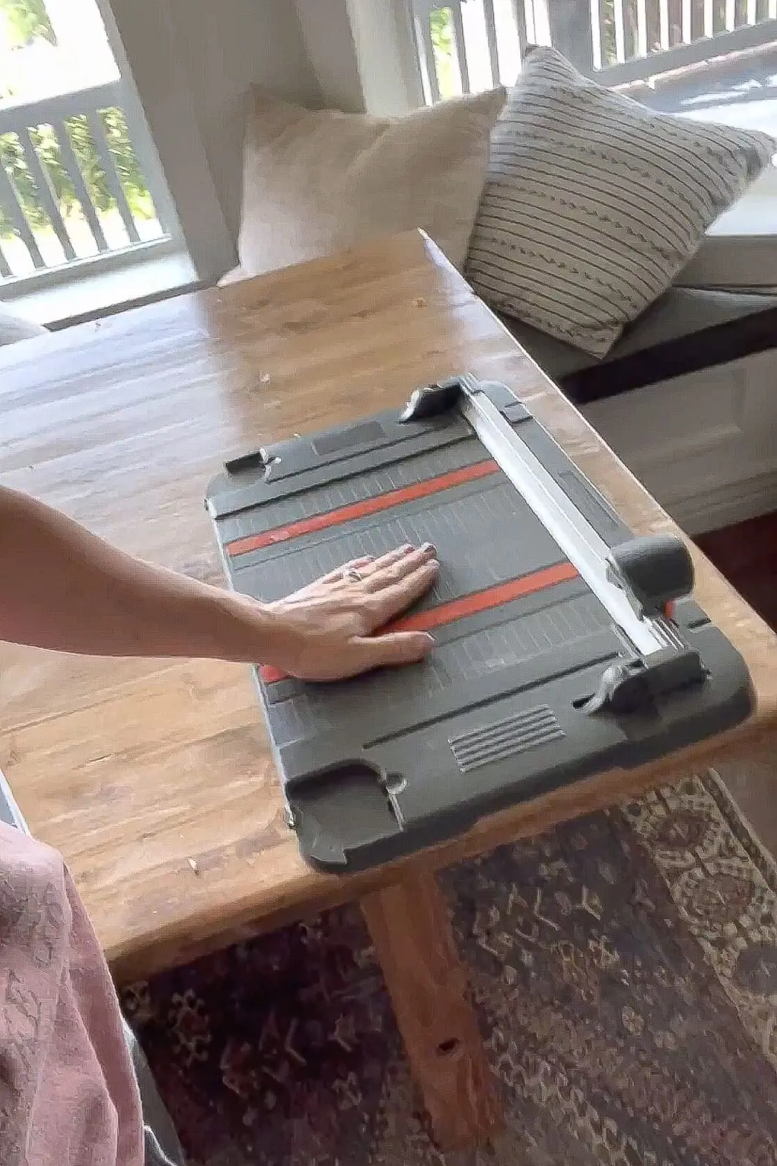 Cutting black vinyl strips with a paper cutter on a wooden table to prep for DIY black window grid installation.